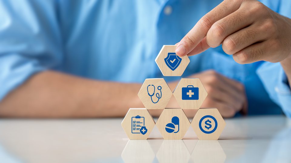 A hand places the top tile on a pyramid of wooden hexagons printed with blue health-care icons.